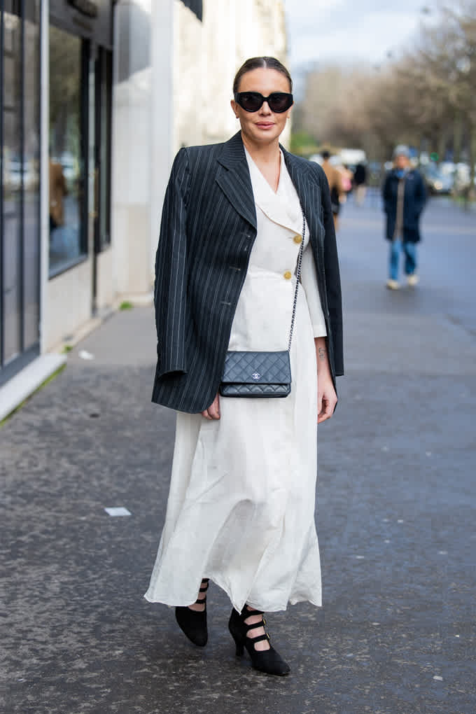 Frau in weißem Kleid trägt einen schwarzen Oversize-Blazer, kombiniert mit einer schwarzen Sonnenbrille