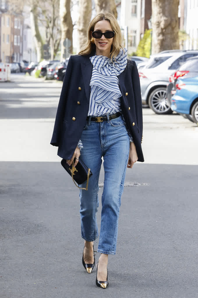 Frau spaziert in Denim-Outfit, trägt Denim-Blazer mit gestreifter Bluse und blauer Jeanshose