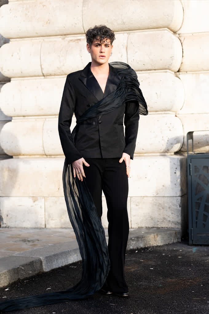 Mann mit schwarzem Hemd und passender Hose, steht lässig vor Steinwand