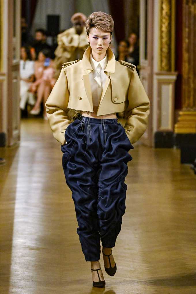 Frau in avantgardistischem Outfit, goldfarbene Jacke mit blauer Haremshose und Heels