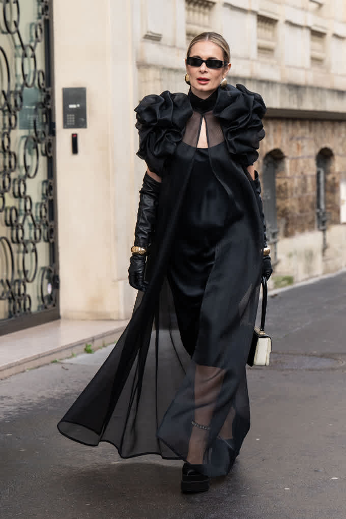 Frau in elegant-schwarzem Kleid, kombiniert mit passenden Handschuhen und Sonnenbrille