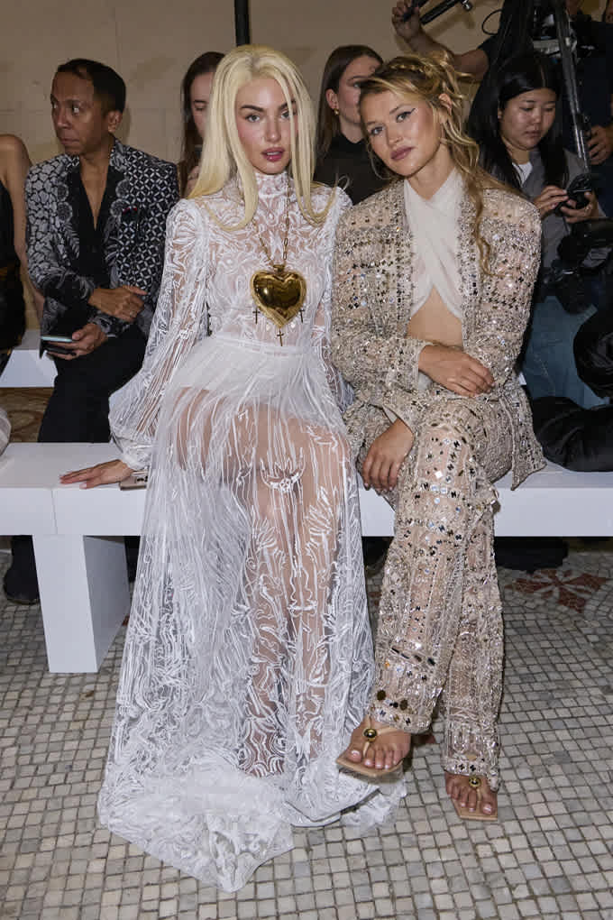 Zwei Frauen in aufwändig gefertigten Kleider-Kombinationen mit Glitzer, sitzend auf weißer Bank