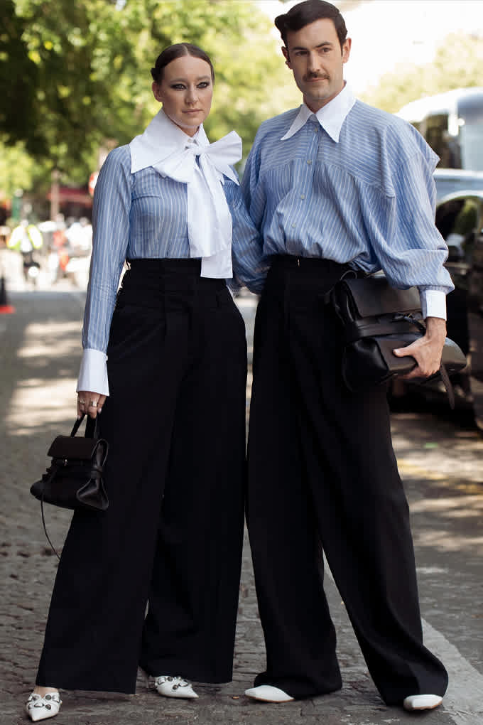 Mann und Frau in passenden Outfits, mit schwarzer Palazzohose, blauem Hemd und weißem Schal / Kragen