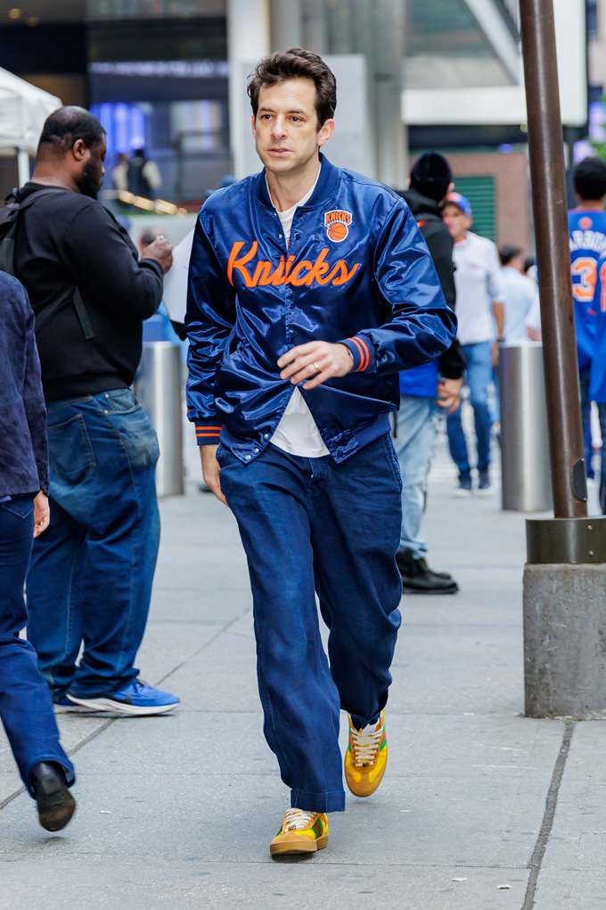 Ein Mann trägt eine blaue Knicks-Collegejacke, eine blaue Jeans, ein weißes Shirt und gelbe Sneaker