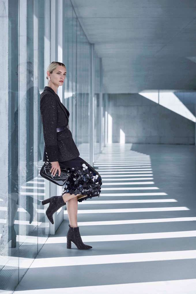 Eine Frau trägt ein elegantes schwarzes Outfit mit Glitzerblazer, einem Rock mit Pailletten und passenden Stiefeletten