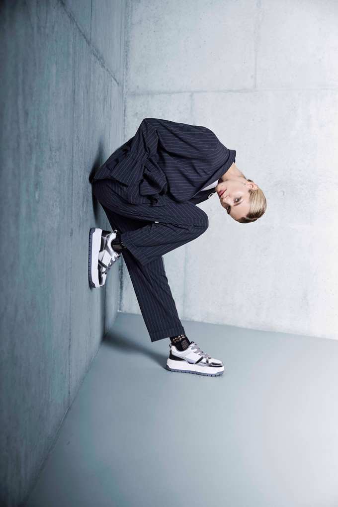 Eine Frau ist nach vorne gebeugt und trägt einen dunkelblauen Hosenanzug mit feinen Streifen und sportlichen Sneakern