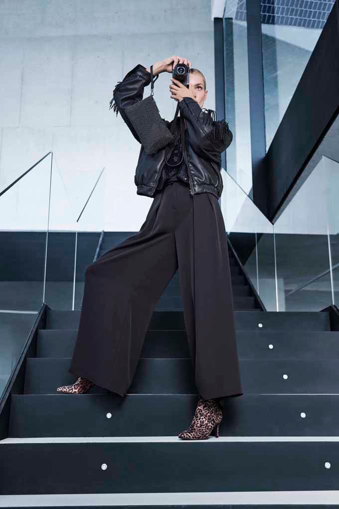 Eine Frau trägt eine schwarze Lederjacke mit Fransen, eine weite Hose und Leo-Stiefeletten.