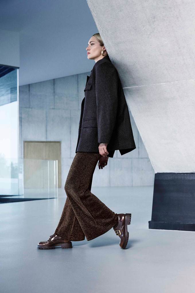 Eine Frau trägt ein dunkles Sakko, eine braune Schlaghose und schwarze Loafer.