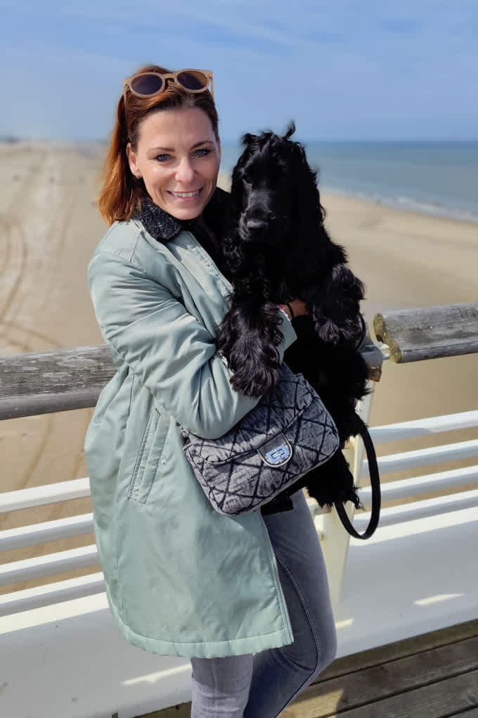 Donna con un cappotto color salvia e un cane nero in braccio