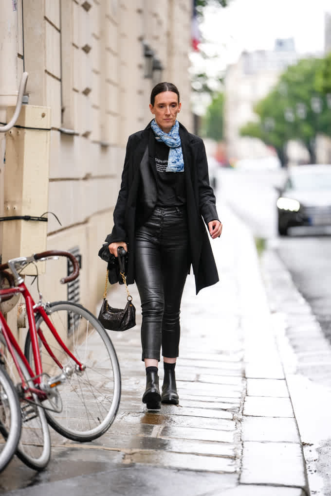 Frau in eleganter Lederhose in Schwarz, kombiniert mit Mantel Ankle Boots und Handtasche
