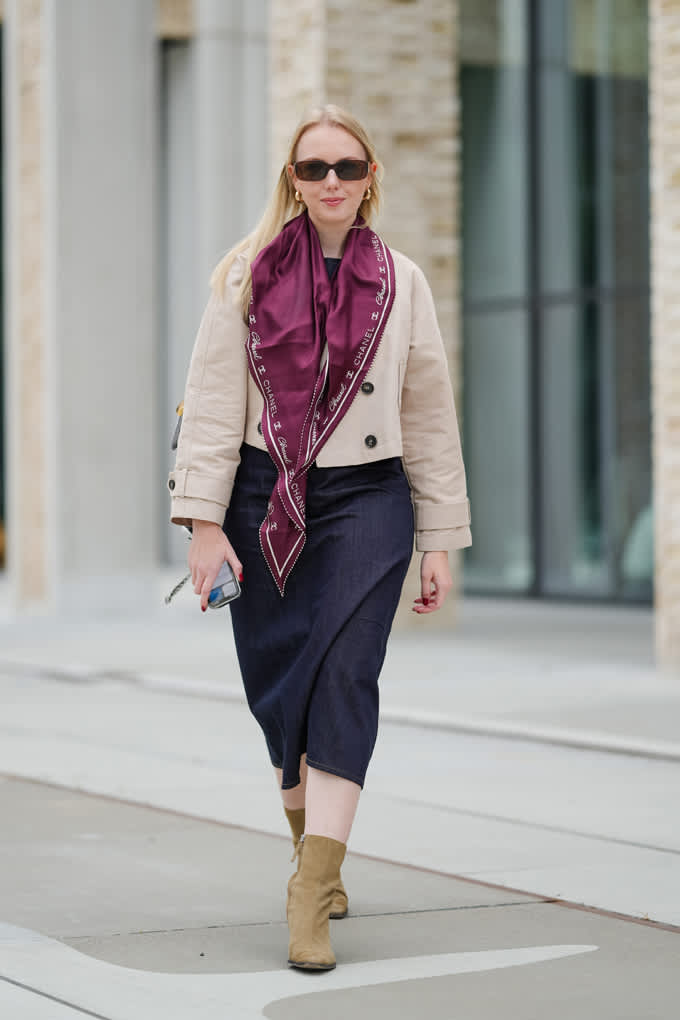 Frau mit beigem Blazer mit beerenfarbenem Halstuch, blauer Hose und braunen Boots