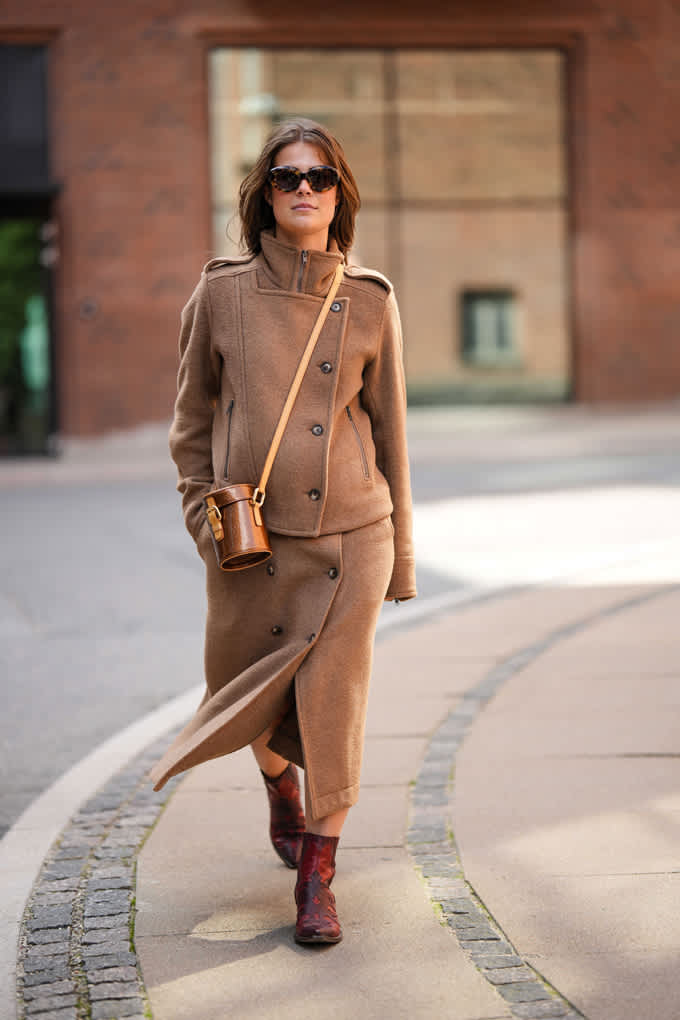 Frau spaziert in hellbraunem Mantel und passendem Wickelrock, trägt dazu Crossbody-Bag
