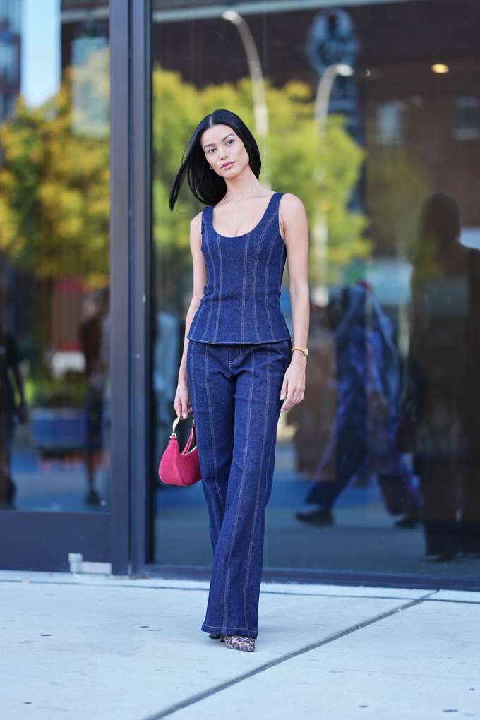Donna in look denim blu scuro, in piedi davanti a una facciata in vetro