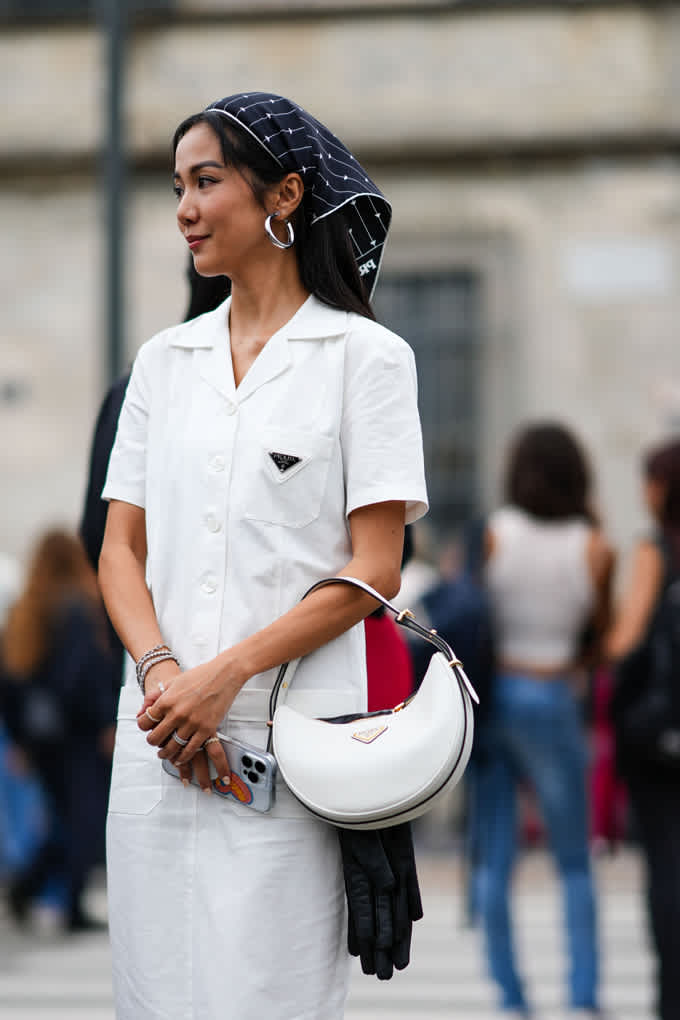 Donna in abito bianco con foulard, con un'elegante borsa bianca a mezzaluna al braccio
