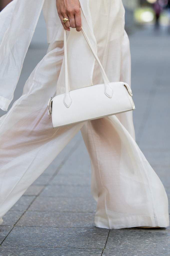 Frau in weißem Outfit trägt farblich passende Baguette Bag in der Hand