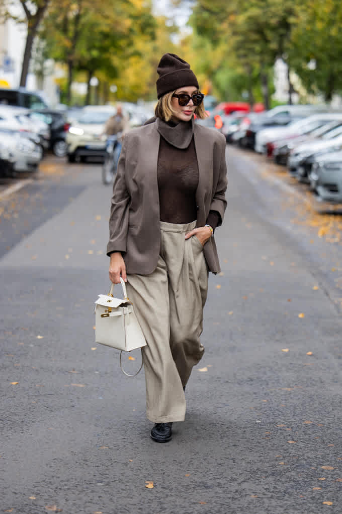 Frau in monochromem Look mit brauner Jacke, dunklem Top und beiger Bundfaltenhose