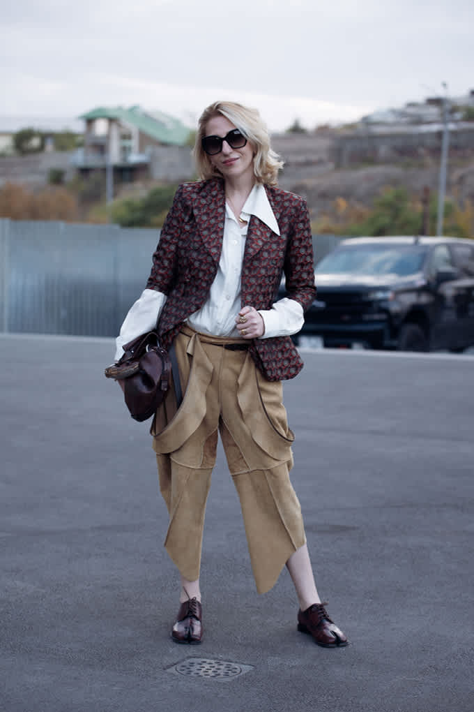 Frau auf Parkplatz trägt Blazer mit Paisleymuster, weiße Hemdbluse und Wildlederhose in Cognac 