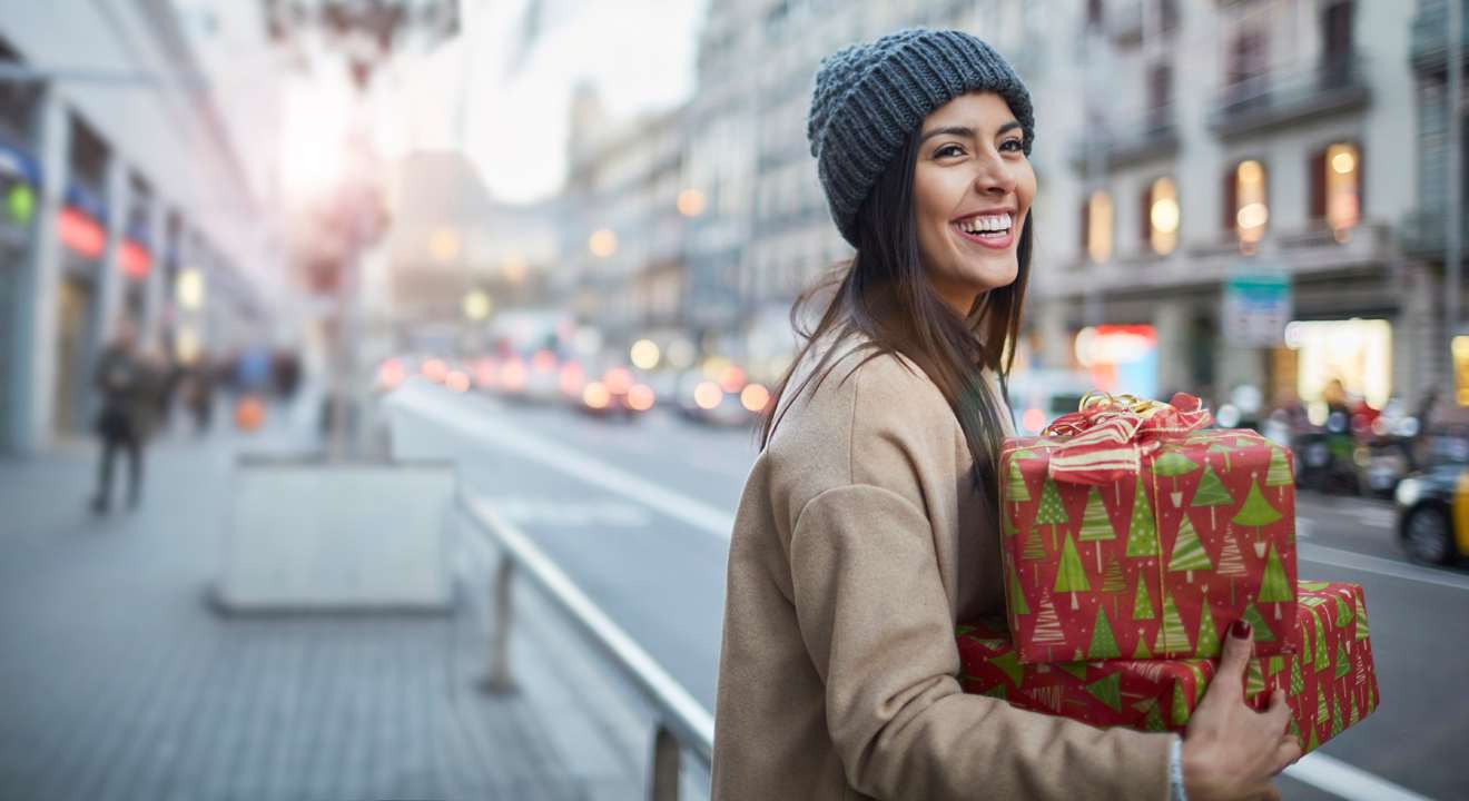 Lächelnde Frau mit Weihnachtsgeschenken in den Armen, stehend in Stadtkulisse