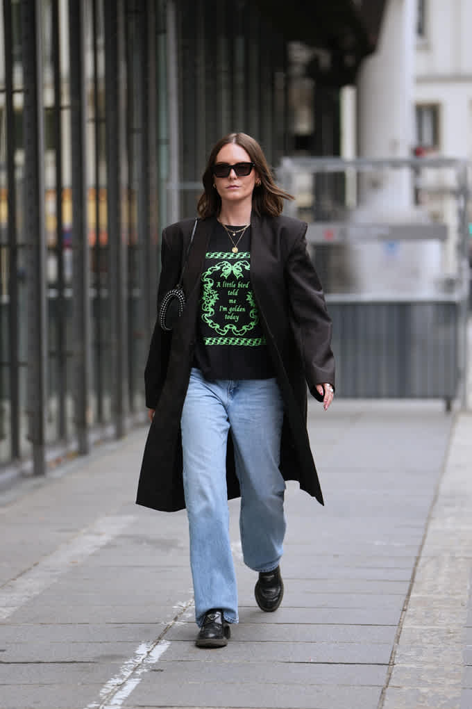 Frau in Grunge-Outfit, spaziert in Look mit Blazer, Logo-Shirt und Jeanshose