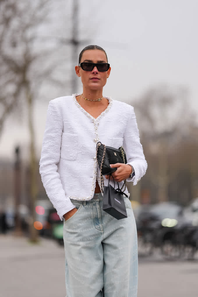 Frau trägt weiße Bouclé-Jacke, kombiniert mit Baggy Denim-Jeans und schwarzer Clutch