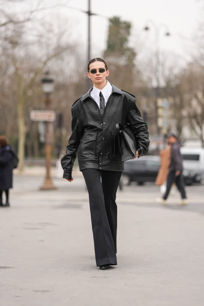 Frau in Matrix Look, kombiniert Lederjacke, weiße Krawatte, oversized Kragen und weite Pants mit schwarzer Ledertasche