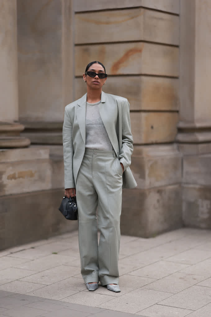 Frau in zart-pistazienfarbenem Soft Suit, posiert vor Steinfassade 