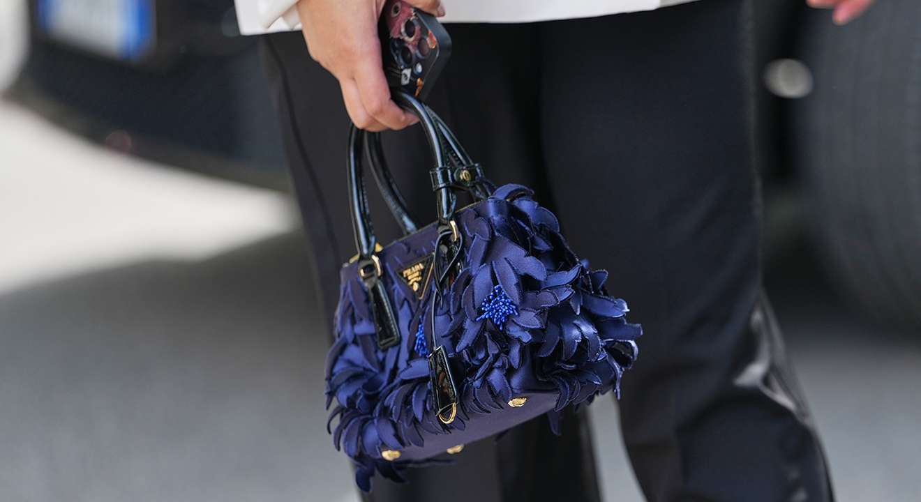 Frau trägt blau-schwarze Handtasche mit Gold-Aufsätzen