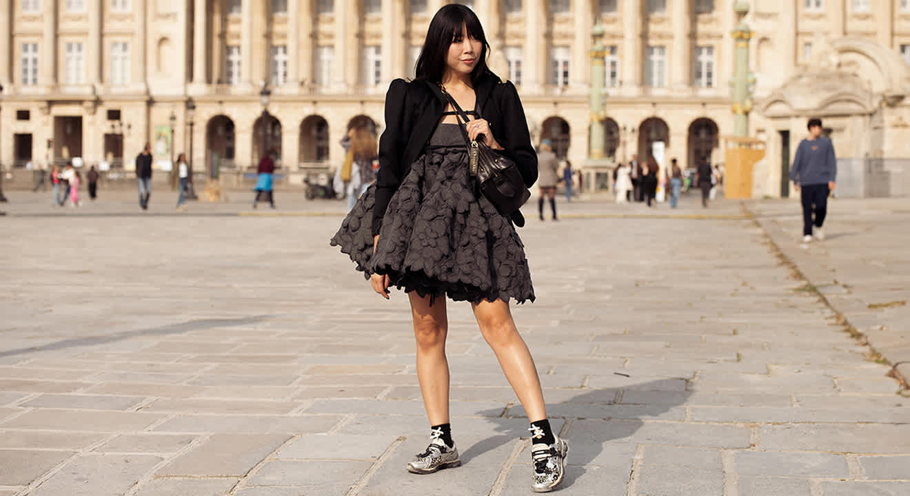 Frau auf großem Platz, trägt schwarzen Blazer mit Kleid und Sneakern