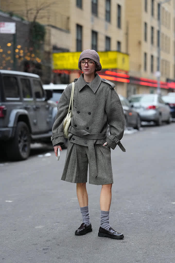 Frau in grauer Tweedjacke mit passendem Skirt im Preppy-Look, steht auf Straße