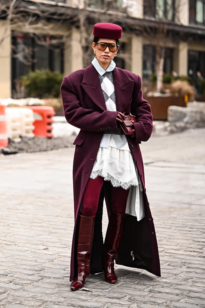 Frau trägt burgunderfarbenen Mantel mit weißem Argyle-Pullunder im Preppy Styöe