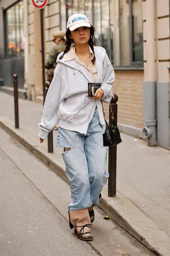 Frau spaziert auf Straße, trägt grauen Zip-Hoodie zu Baggy Jeans und Cap im Tomboy Style