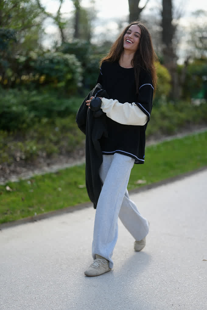 Dunkelhaarige Frau spaziert, trägt schwarzen Sweater und hellblaue Jeanshose im Tomboy Style