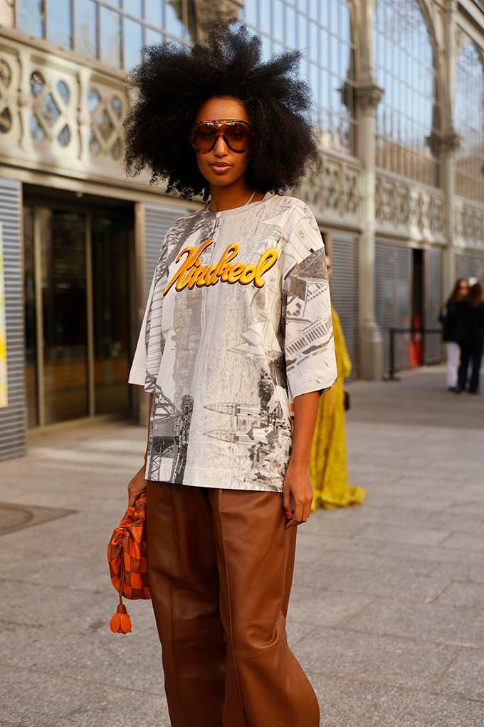 Stark gebräunte Frau mit Afro, trägt weites Print-Shirt mit orange-roter Lederhose