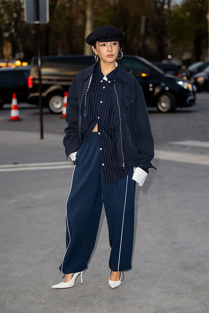 Frau in Nadelstreifen-Anzug und Hose, mit schwarzer Cap und weißen Heels für den Tailoring Look