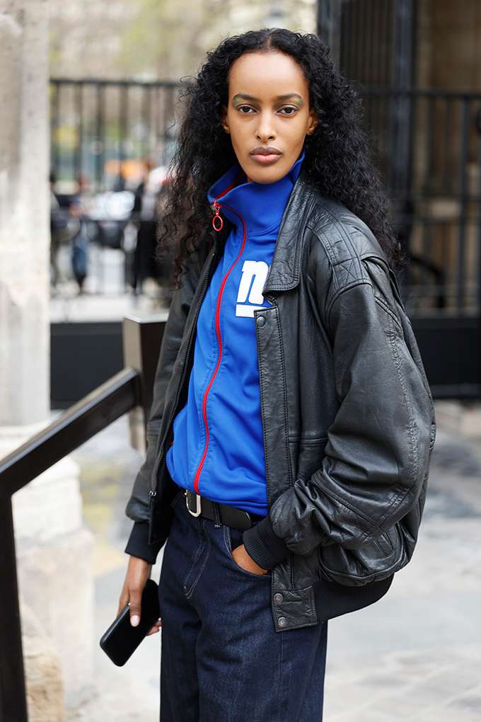 Frau mit lockigen schwarzen Haaren, trägt blaues Track-Jacket unter Lederjacke