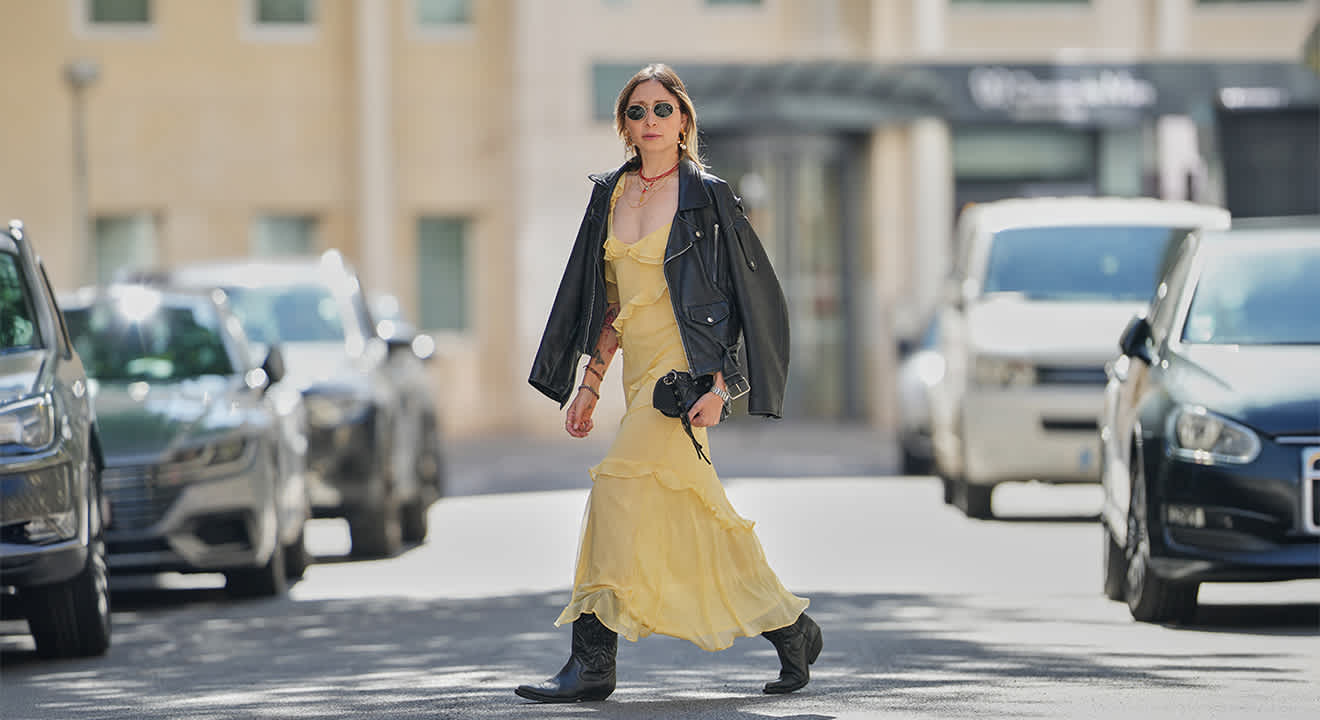 Frau in gelbem Kleid mit Lederjacke und Cowboy Boots, spaziert auf Straße