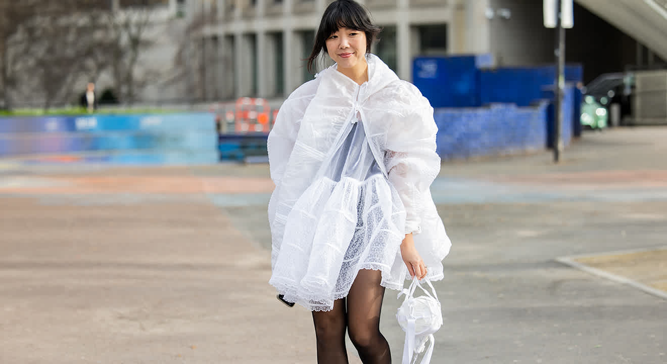 Schwarzhaarige Frau in weißem, halbtransparenten Dress, in urbaner Kulisse