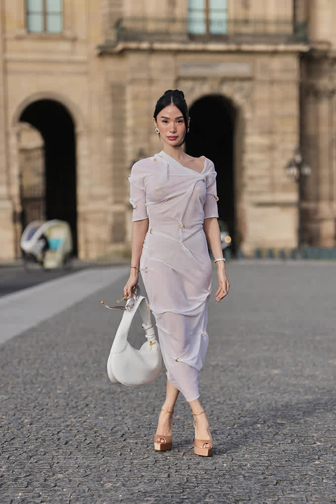 Frau in transparentem Dress-Look in Rosa, mit braunen Sandaletten, trägt weiße Handtasche