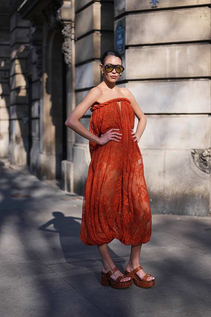 Frau mit schwarzer Sonnenbrille und rotem Sheer Dress, posiert vor Steinmauer