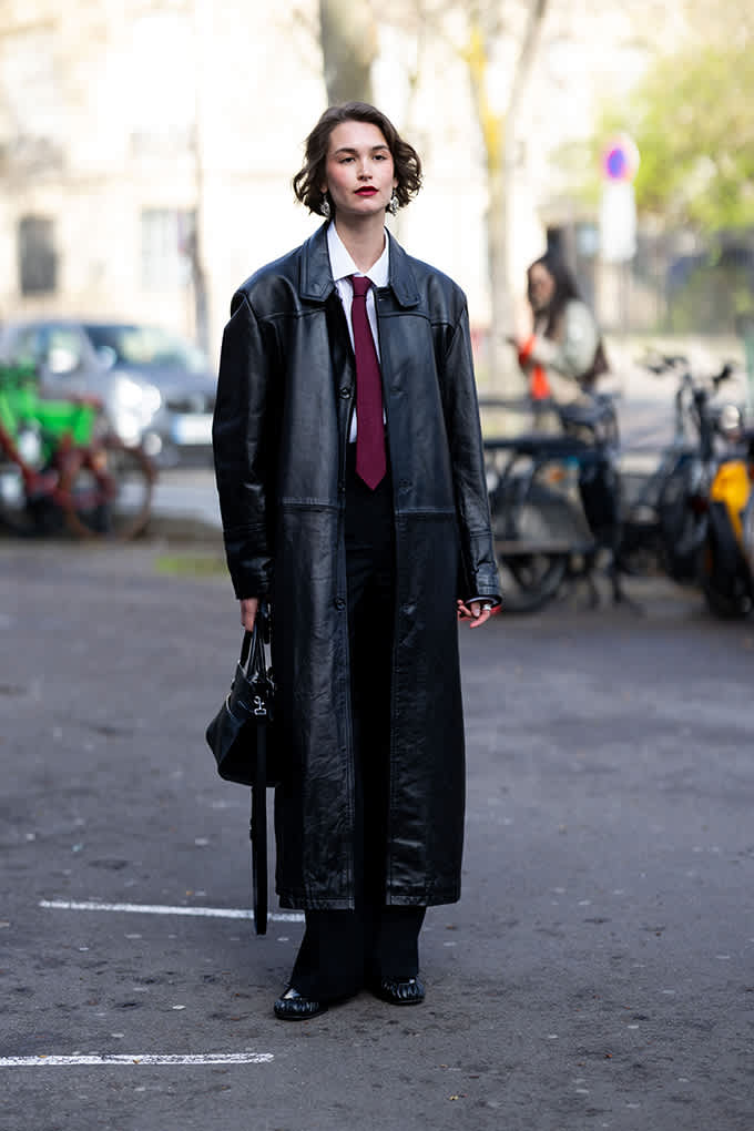 Frau in Fluid Fashion-Menswear-Coat, trägt rote Krawatte und Clutch