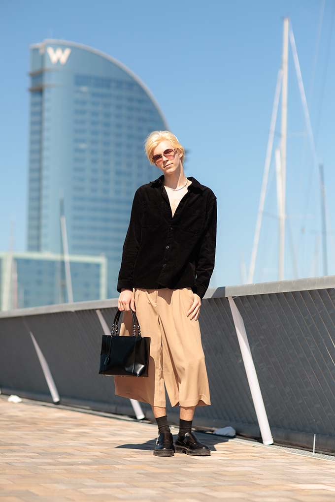 Blonde Frau mit schwarzem Hemd und Midirock, steht vor Hochhaus in Dubai