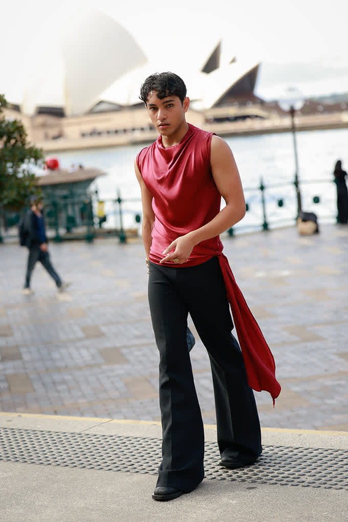 Mann trägt rotes Satin-Top mit schwarz-ausgestellter Hose, spaziert auf Bürgersteig