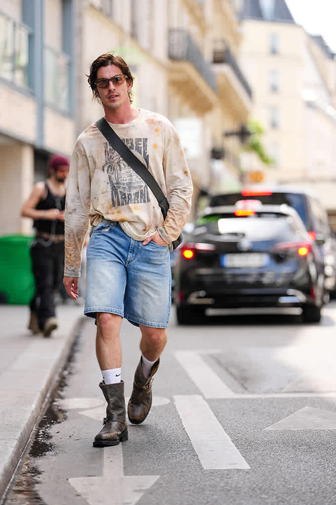 Mann läuft mit braunen Bikerboots, Denim-Shorts und Longsleeve über die Straße