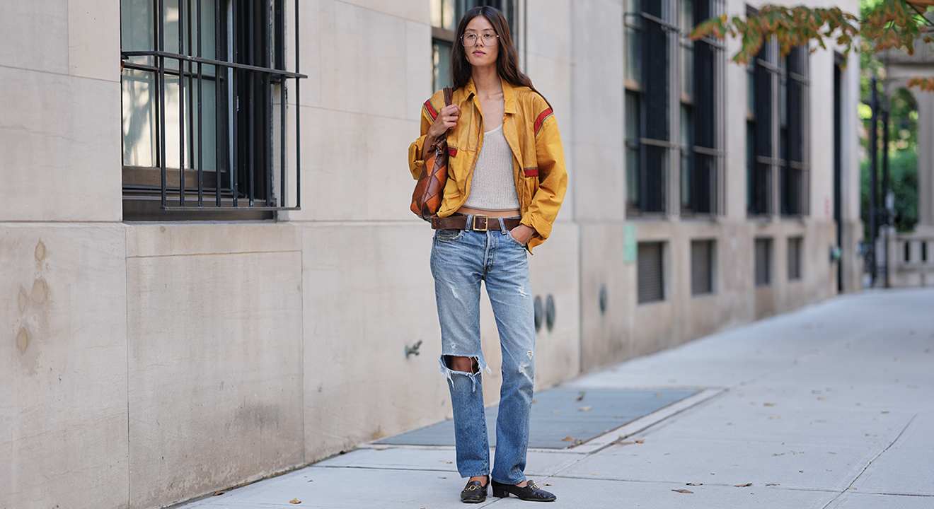 Frau in gelber Retro-Jacke und Used Jeans vor Hauswand