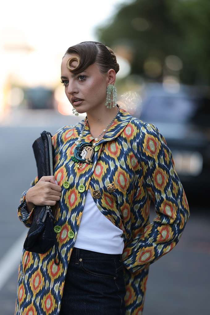 Frau mit curly Haaren, steht auf Straße trägt Ikat-Bolero und Vintage-Tasche