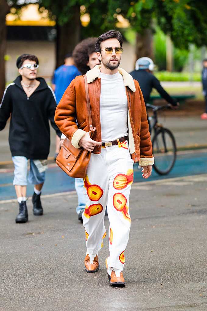 Mann mit brauner Seitentasche, trägt Shearling-Aviatorjacke mit weißer Pop-Print-Hose