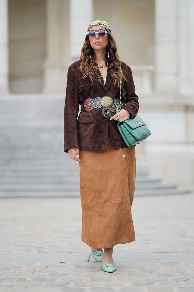 Frau kombiniert braunen Suede-Blazer, Concho-Gürtel und sandfarbenen Maxi-Rock zu Retro-Outfit