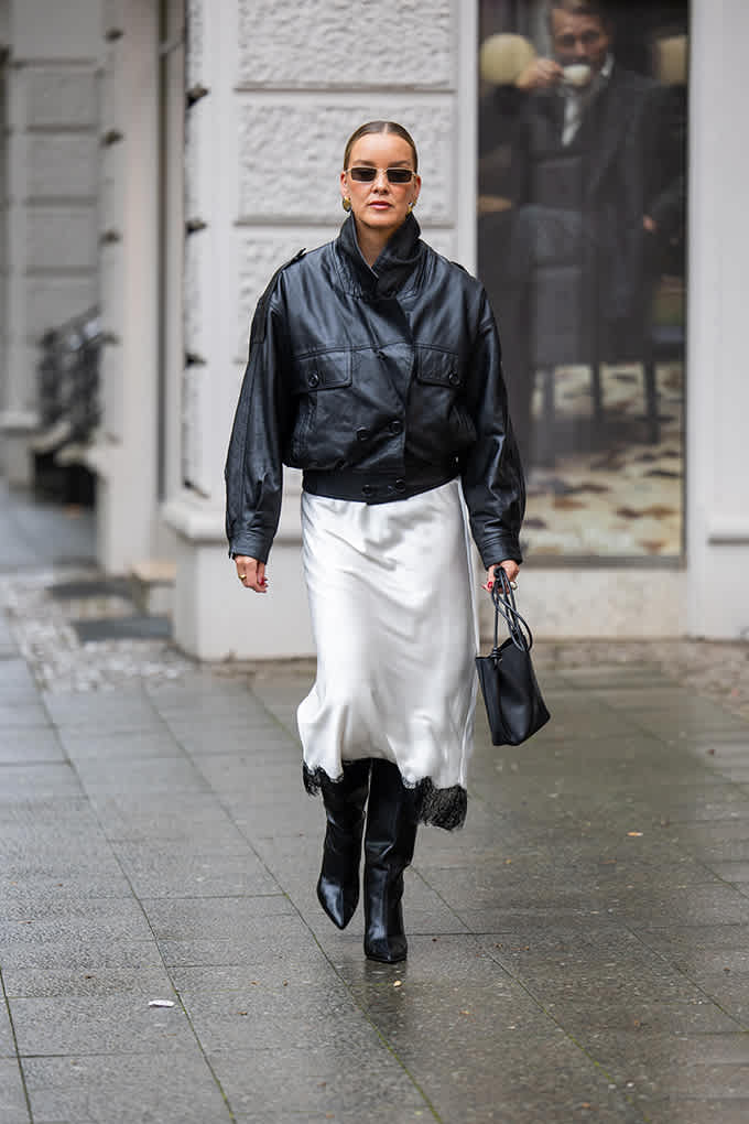 Frau kombiniert schwarze Bomberjacke mit hellem Slip-Rock zum Retro-Outfit