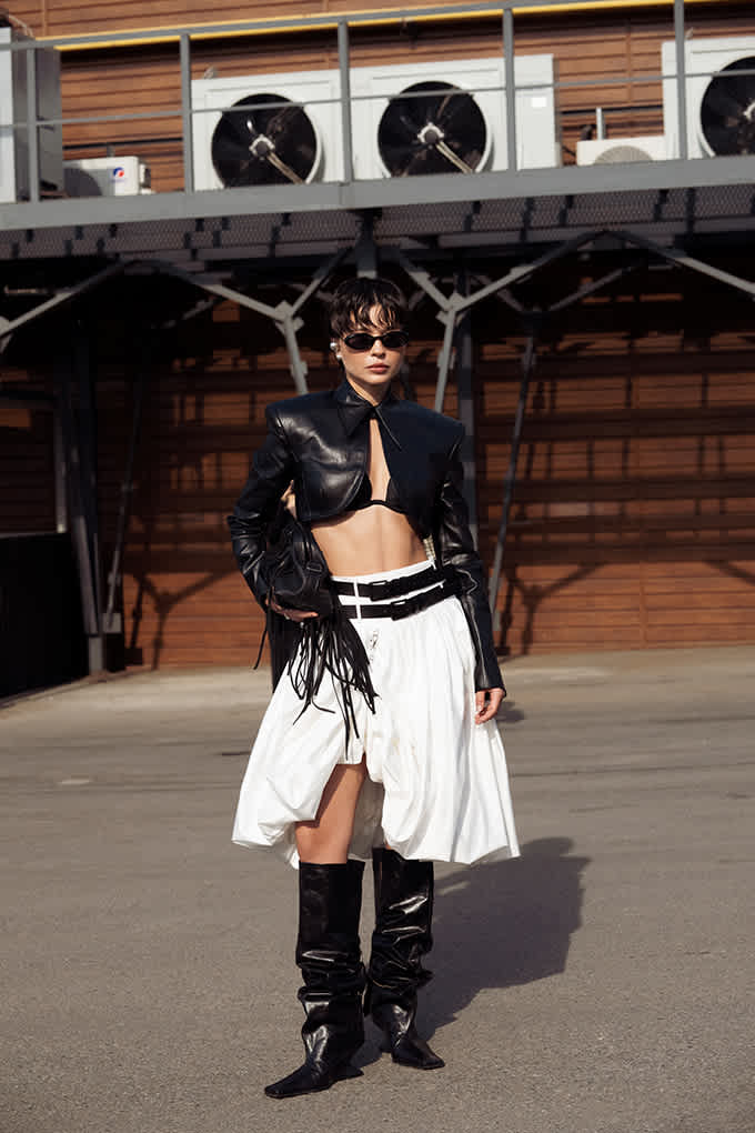 Schwarzhaarige Frau trägt kurze Lederjacke, kombiniert mit Weißem Rock mit Multi-Belt und Cowboyboots