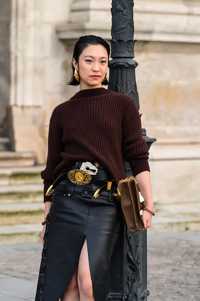 Asiatische Frau mit rotem Strickpullover und schwarzem Lederrock, trägt mehrere Gürtel übereinander